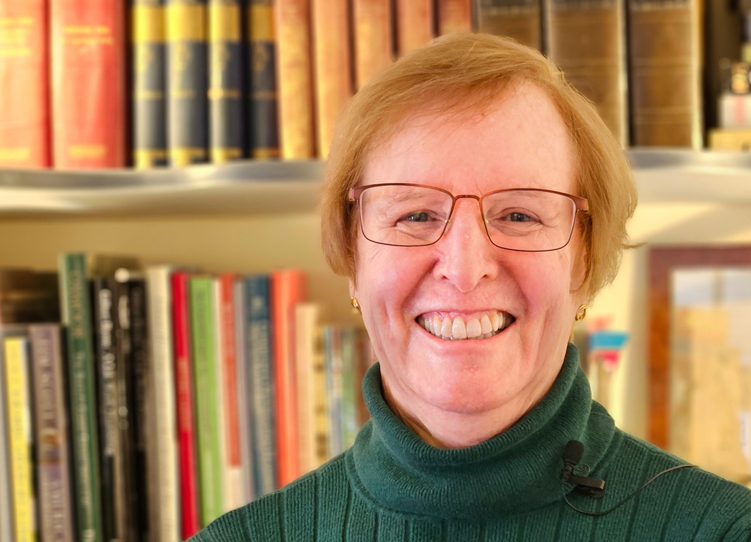 A woman with glasses smiling in front of some books.
